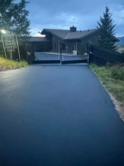 Newly paved black asphalt driveway with metal gates at residential home entrance