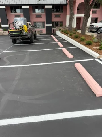 Freshly sealed asphalt parking lot with white and pink striping, directional markings, and equipment on site