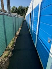 New black asphalt pathway between blue storage units and green fence