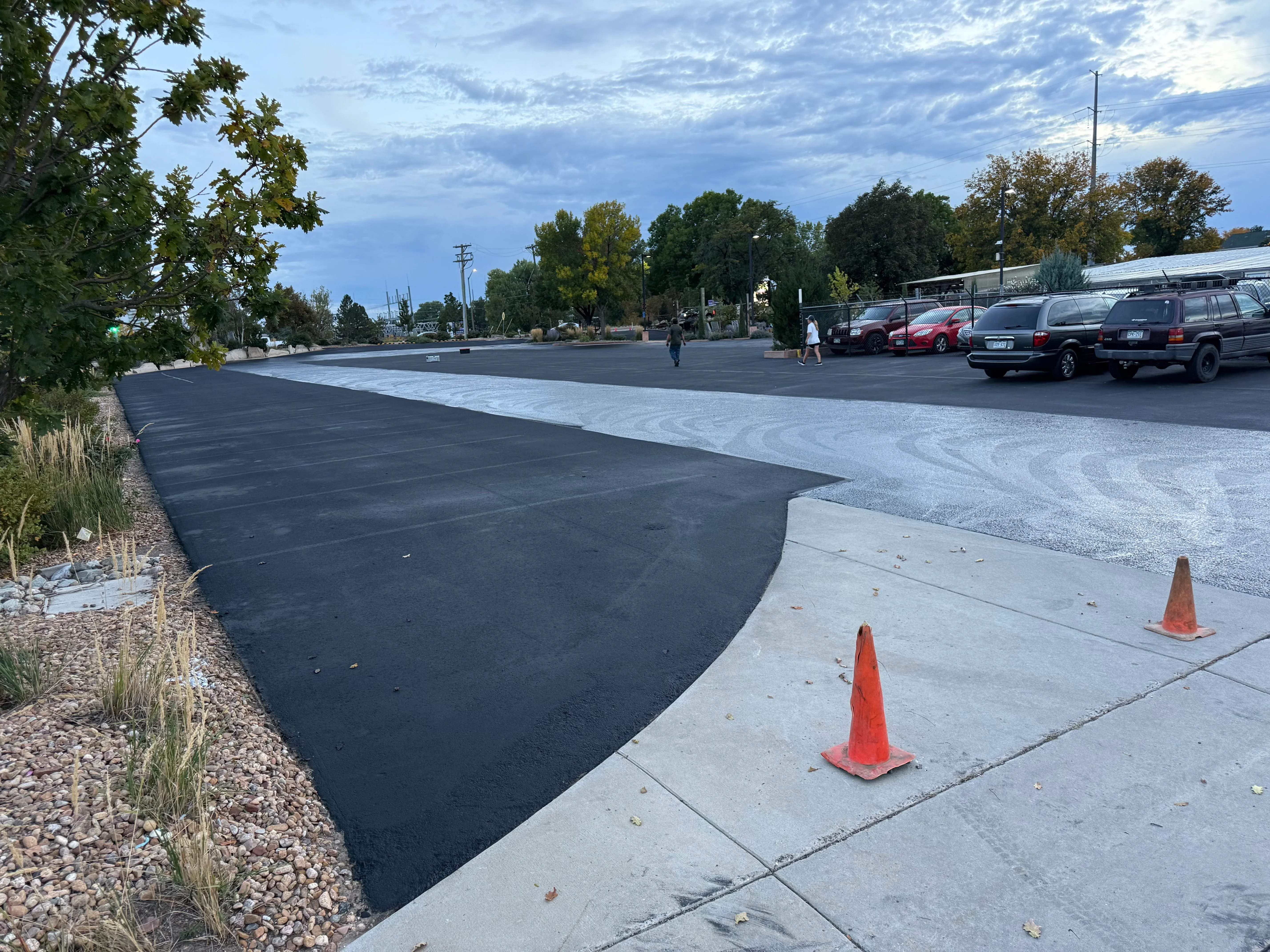 Fresh black asphalt parking lot with concrete curb and sidewalk transitions, gravel landscaping border