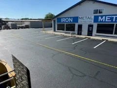 Newly paved commercial asphalt parking lot with yellow parking space lines and metal building storefront