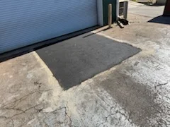 New dark asphalt apron installed at commercial garage entrance with concrete pad