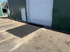 New asphalt patch on commercial parking lot next to green metal building