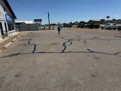 Commercial asphalt parking lot with marked cracks and maintenance crew assessing pavement condition