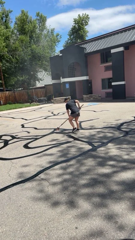 Worker pressure washing commercial asphalt parking lot with multi-story building in background