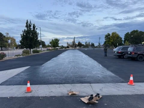 Fresh black asphalt paving with white center stripe and traffic cones on commercial lot